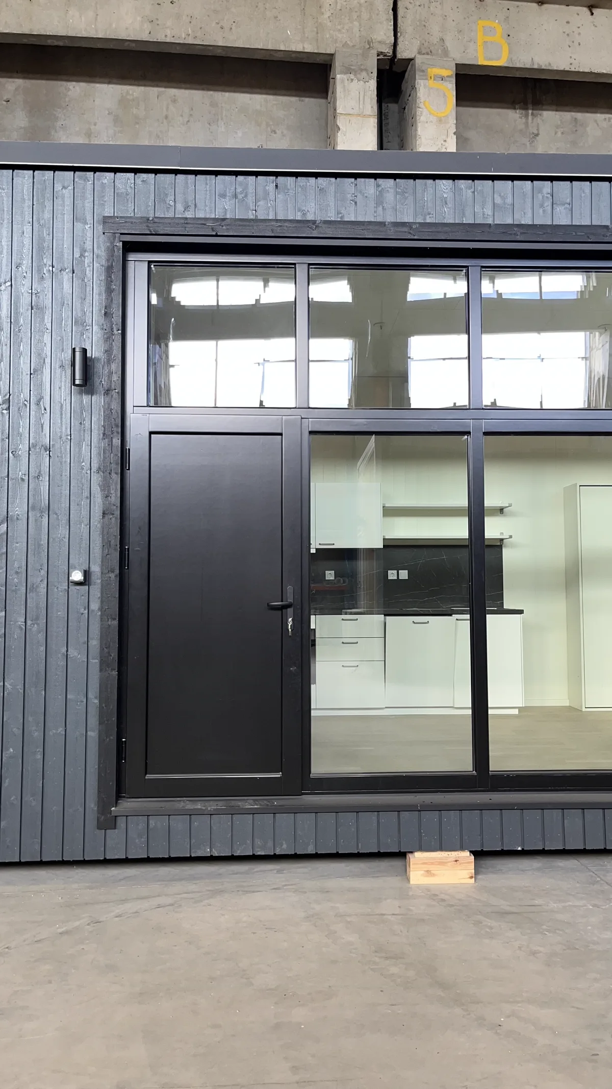 Современная чёрная входная деревянная дверь со стеклянной стеной на тёмно-сером деревянном фасаде