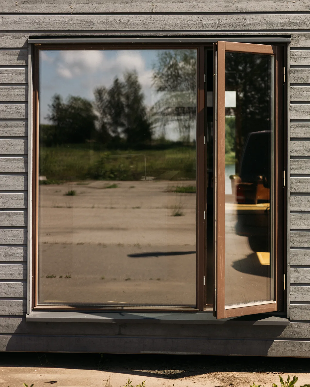 Скандинавское деревянное окно с открыванием наружу - демонстрация открытого положения на сером фасаде