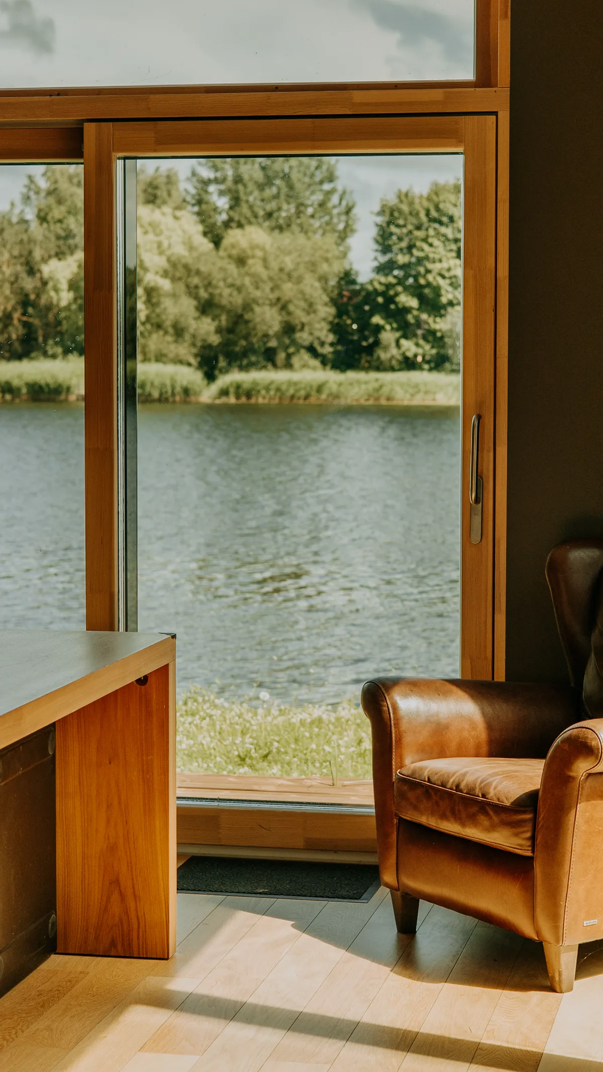 Раздвижная деревянная дверь с видом на озеро, кожаное кресло, натуральная сосновая рама