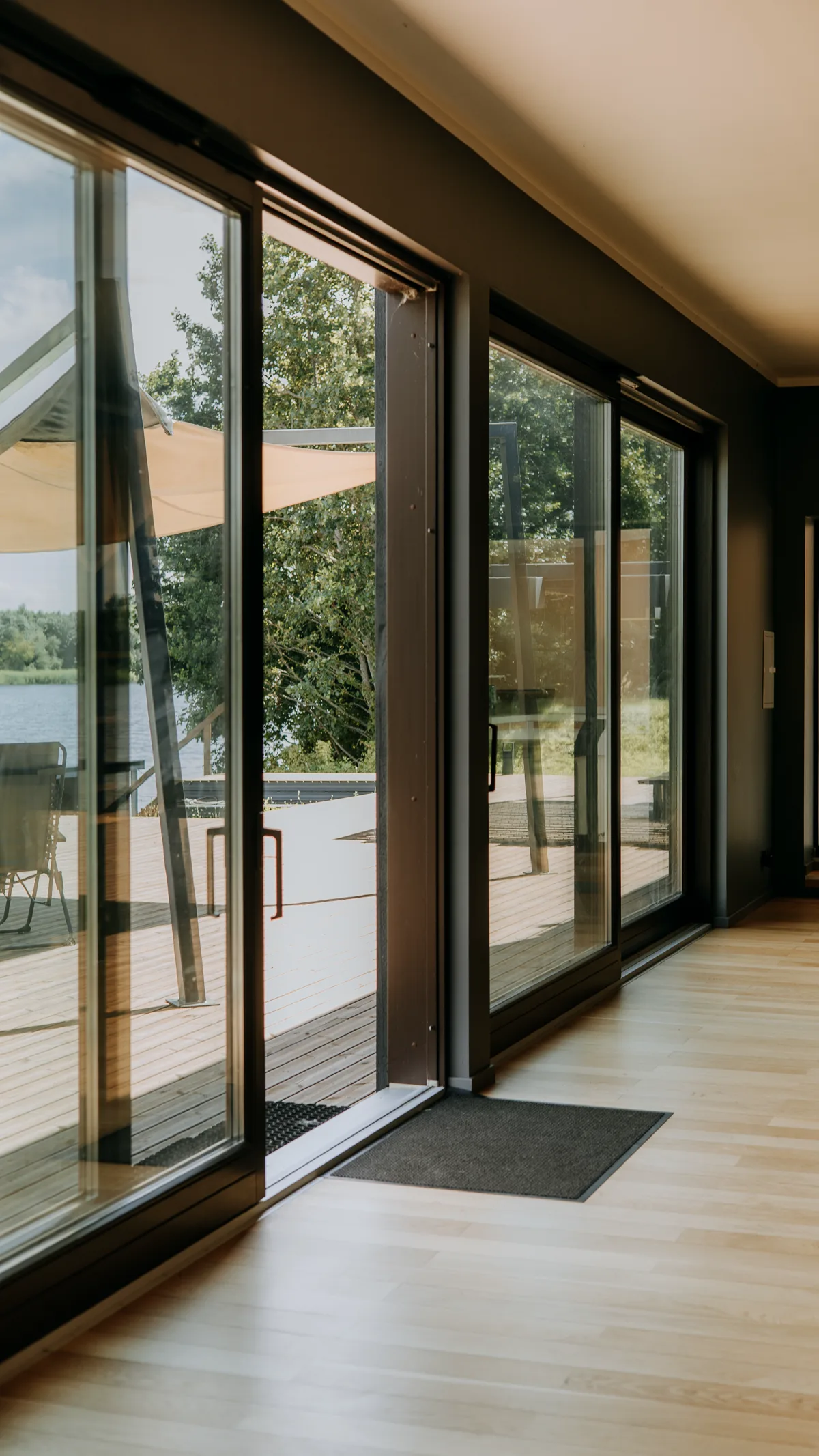 Большие раздвижные деревянные двери открытые на деревянную террасу с садом и видом на озеро