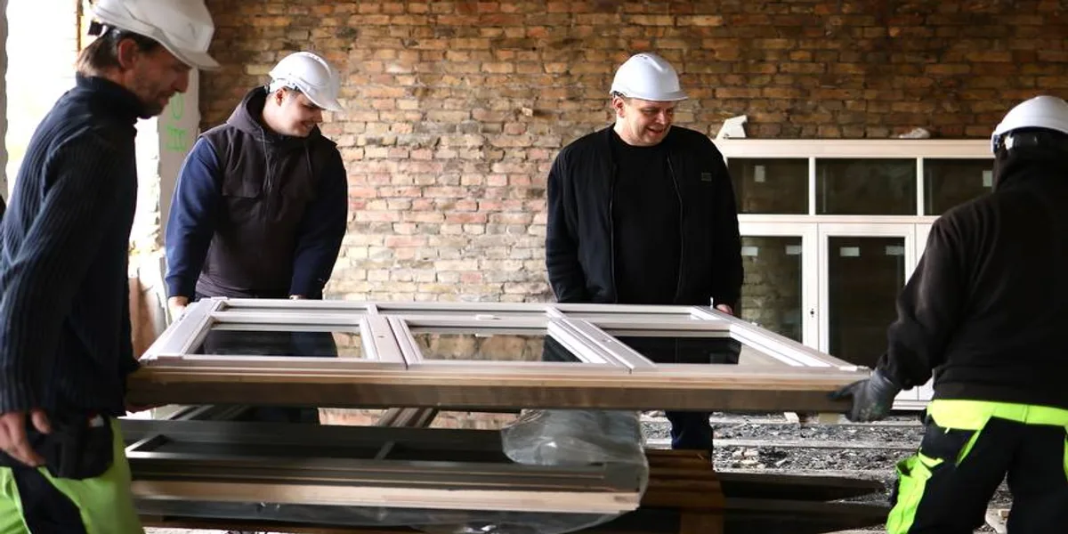Команда монтажа Windows Latvia переносит раму деревянного окна на строительной площадке - установка деревянных окон