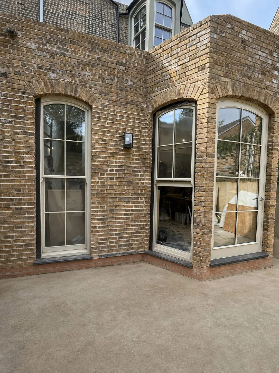 Two tall timber sash windows with semicircular arched heads and 4 over 4 glazing in a brick wall, one lower sash raised