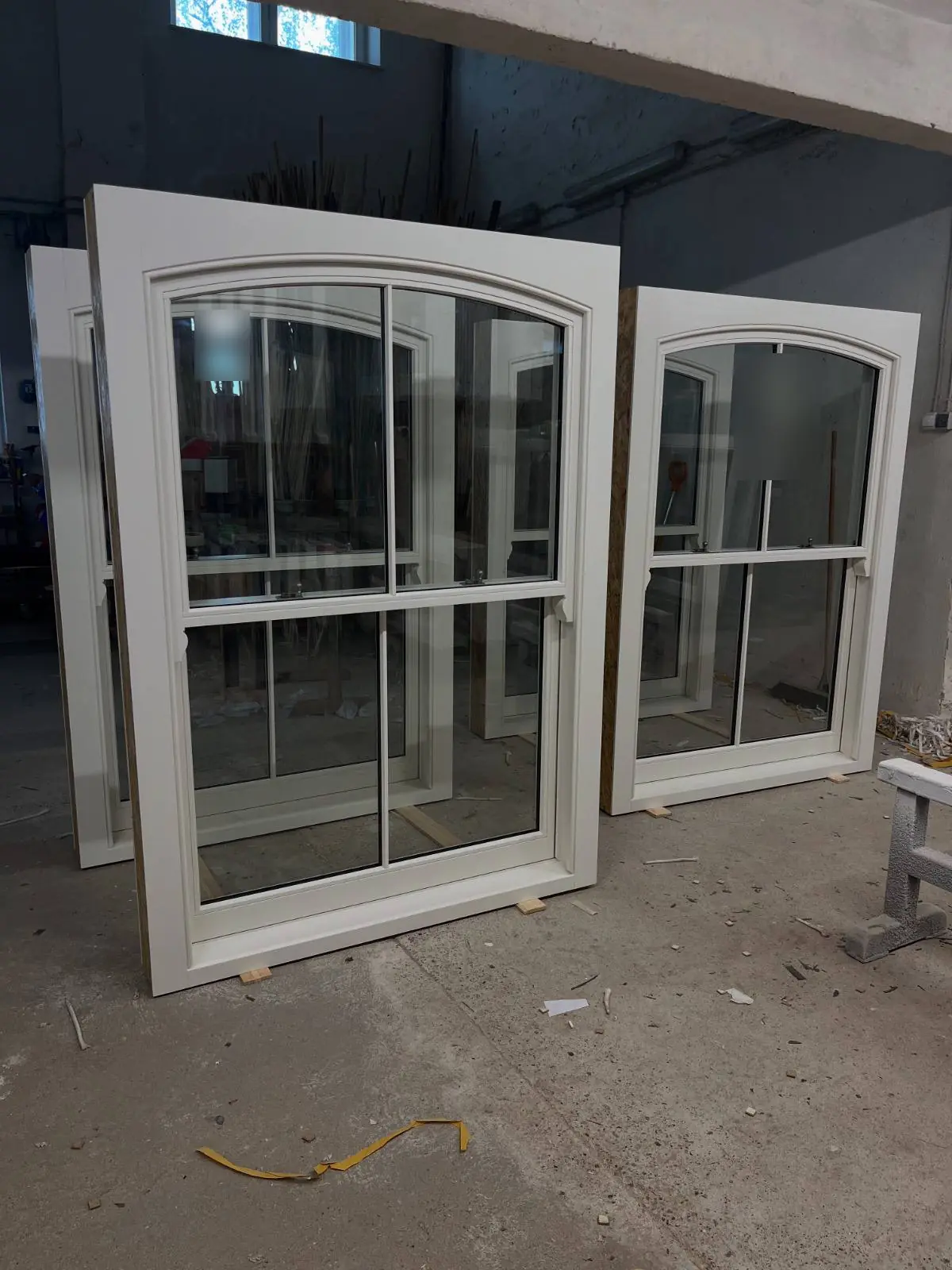 Timber sash windows with segmental arched heads in white primer in the workshop, 2 over 2 glazing, horns and brass fasteners