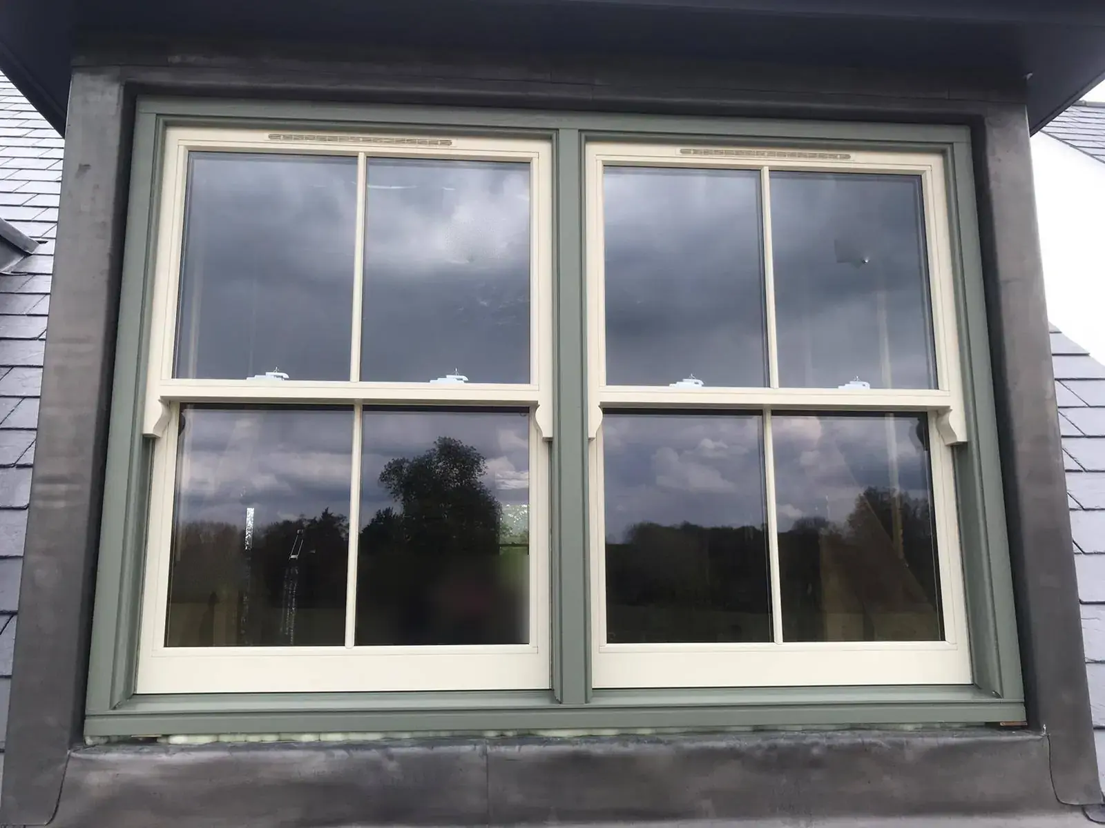 Pair of timber sash windows in a dormer, cream sashes in a green frame, 2 over 2 glazing with trickle vents in the upper sash top rails